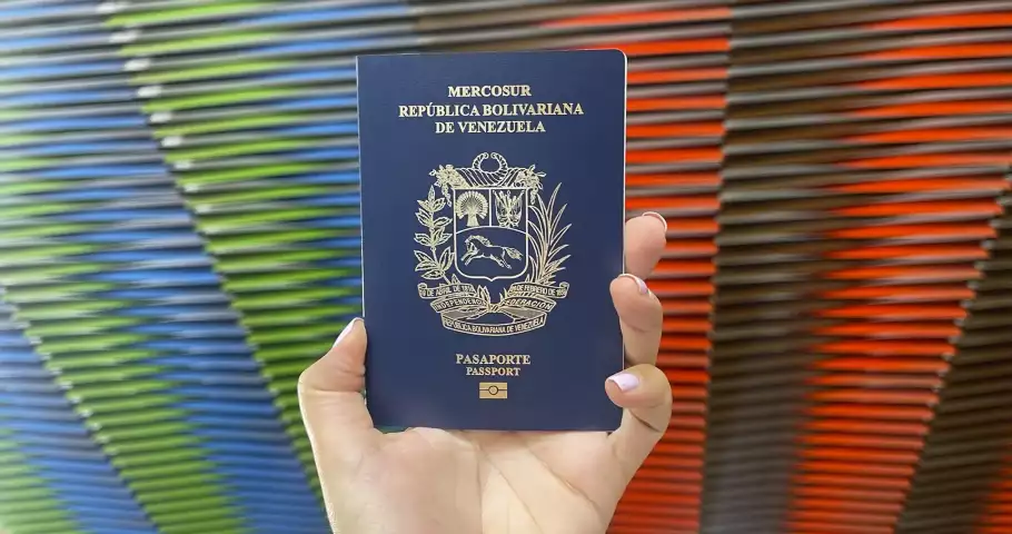 Una mano sostiene un pasaporte venezolano en un fondo de colores
